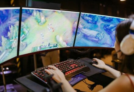 A young woman intently gaming on a multi-screen setup, showcasing vibrant gaming visuals., tags: bankroll management esports - pexel