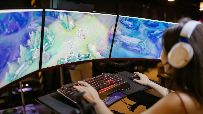 A young woman intently gaming on a multi-screen setup, showcasing vibrant gaming visuals., tags: bankroll management esports - pexel