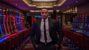 Businessman standing confidently in a luxurious casino with rows of gaming machines., tags: online - pexel