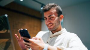 Smiling man using smartphone and laptop in modern office. Connectivity and multitasking concept., tags: smart online casino - pexel