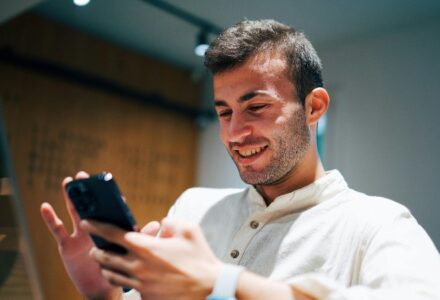 Smiling man using smartphone and laptop in modern office. Connectivity and multitasking concept., tags: smart online casino - pexel