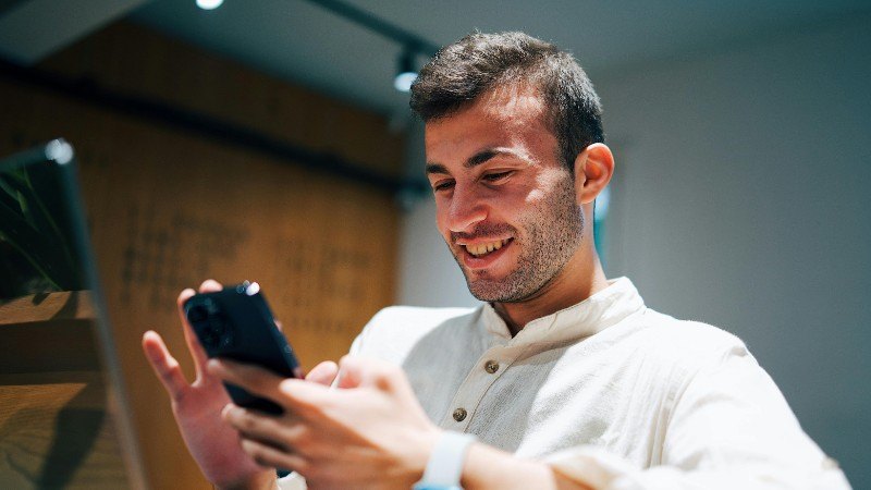 Smiling man using smartphone and laptop in modern office. Connectivity and multitasking concept., tags: smart online casino - pexel