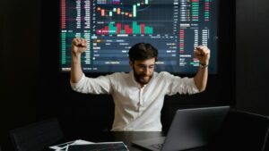 Businessman celebrates stock market success with hands raised in excitement at a trading desk., tags: cs2 - pexel