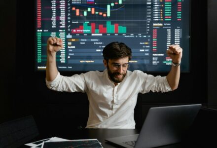 Businessman celebrates stock market success with hands raised in excitement at a trading desk., tags: cs2 - pexel