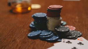 Poker chips stacked on a wooden table with playing cards and blurred glass in the background., tags: ontario’s - pexel