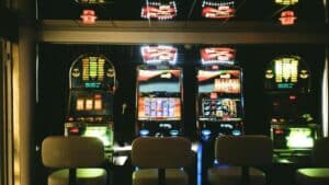 Slot machines in a dimly lit casino with reflective ceiling and empty chairs., tags: money slots - pexel