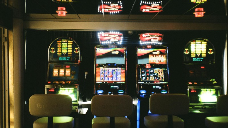 Slot machines in a dimly lit casino with reflective ceiling and empty chairs., tags: money slots - pexel