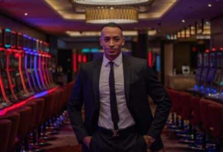 Businessman standing confidently in a luxurious casino with rows of gaming machines., tags: playtech fun, - pexel