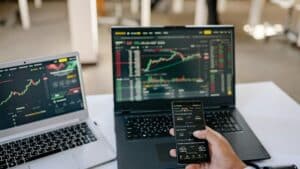 A professional tracks stock market trends using two laptops and a smartphone, showcasing digital finance tools., tags: online gambling - pexel
