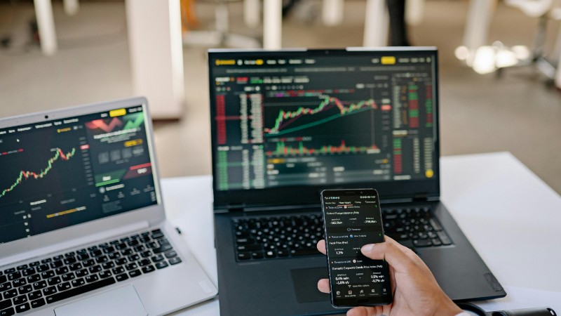 A professional tracks stock market trends using two laptops and a smartphone, showcasing digital finance tools., tags: online gambling - pexel